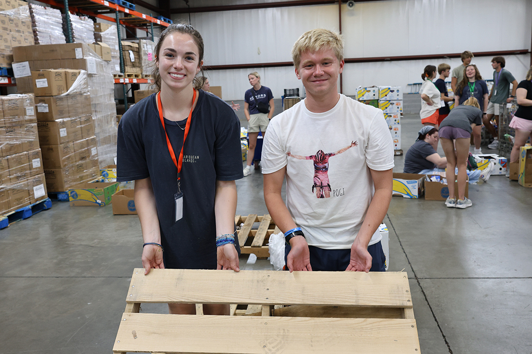 two students holding a pallet of wood at the food bank